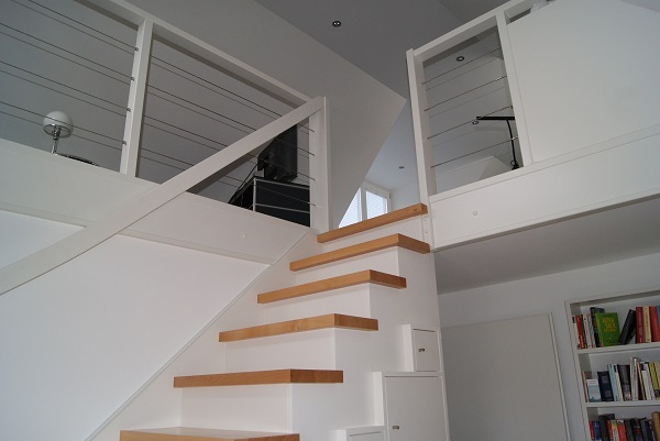 Moderne Holztreppe mit weißem Geländer in heller Maisonette-Wohnung mit Bücherregal.