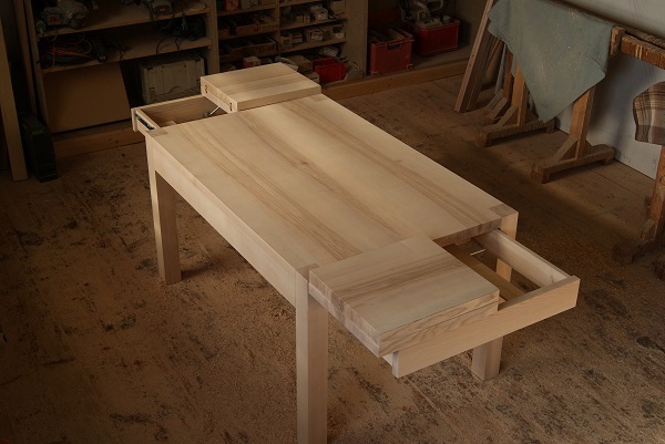 Massiver Holztisch mit Schubladen in einer traditionellen Tischlerwerkstatt auf Holzfußboden.