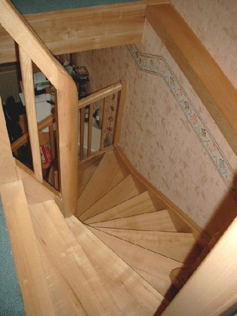 Holztreppe mit Geländer in einem Wohnhaus, enge gewendelte Stufen, helle Holzoptik.